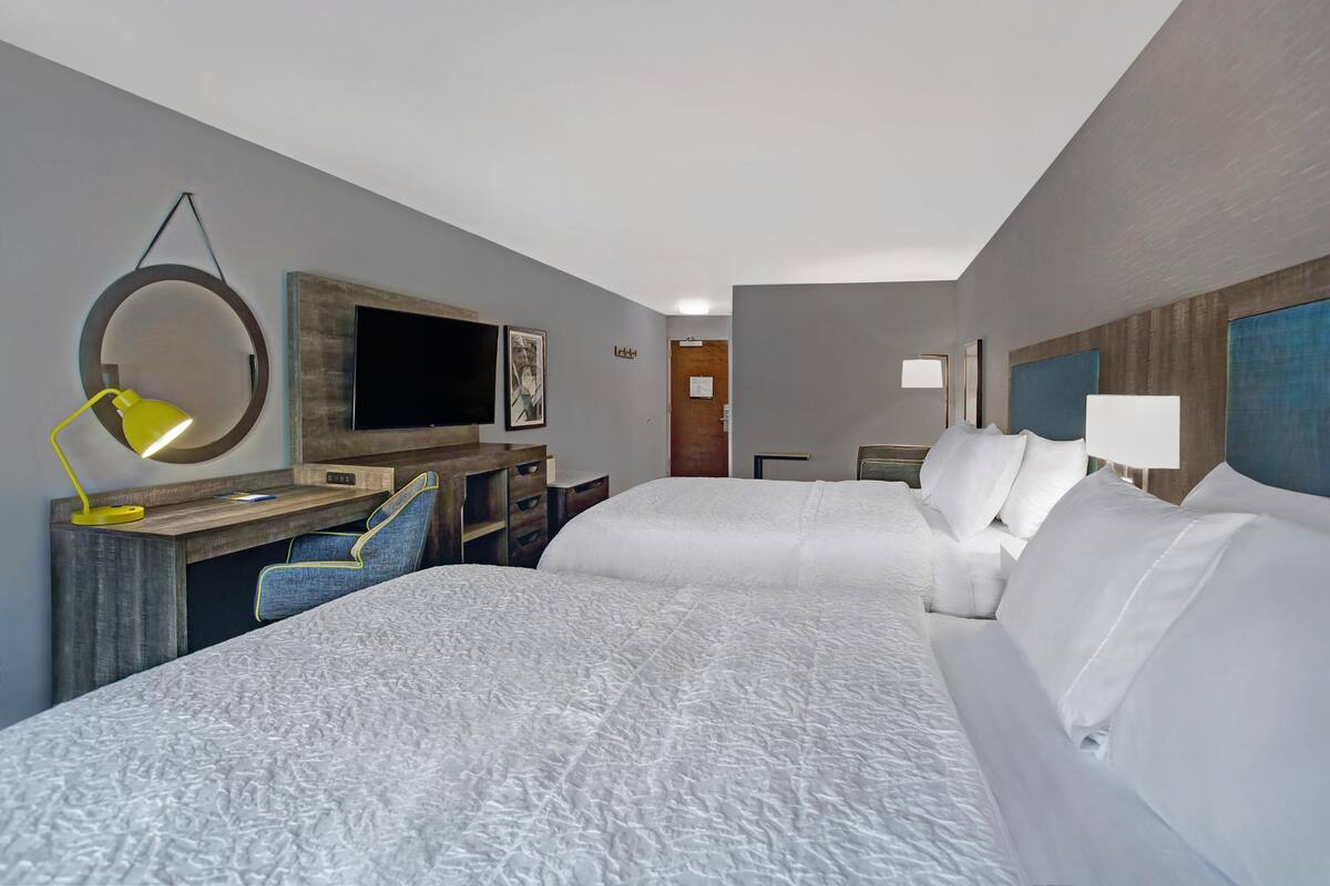 A hotel room with two beds, a desk with a chair, a television, and a mirror.