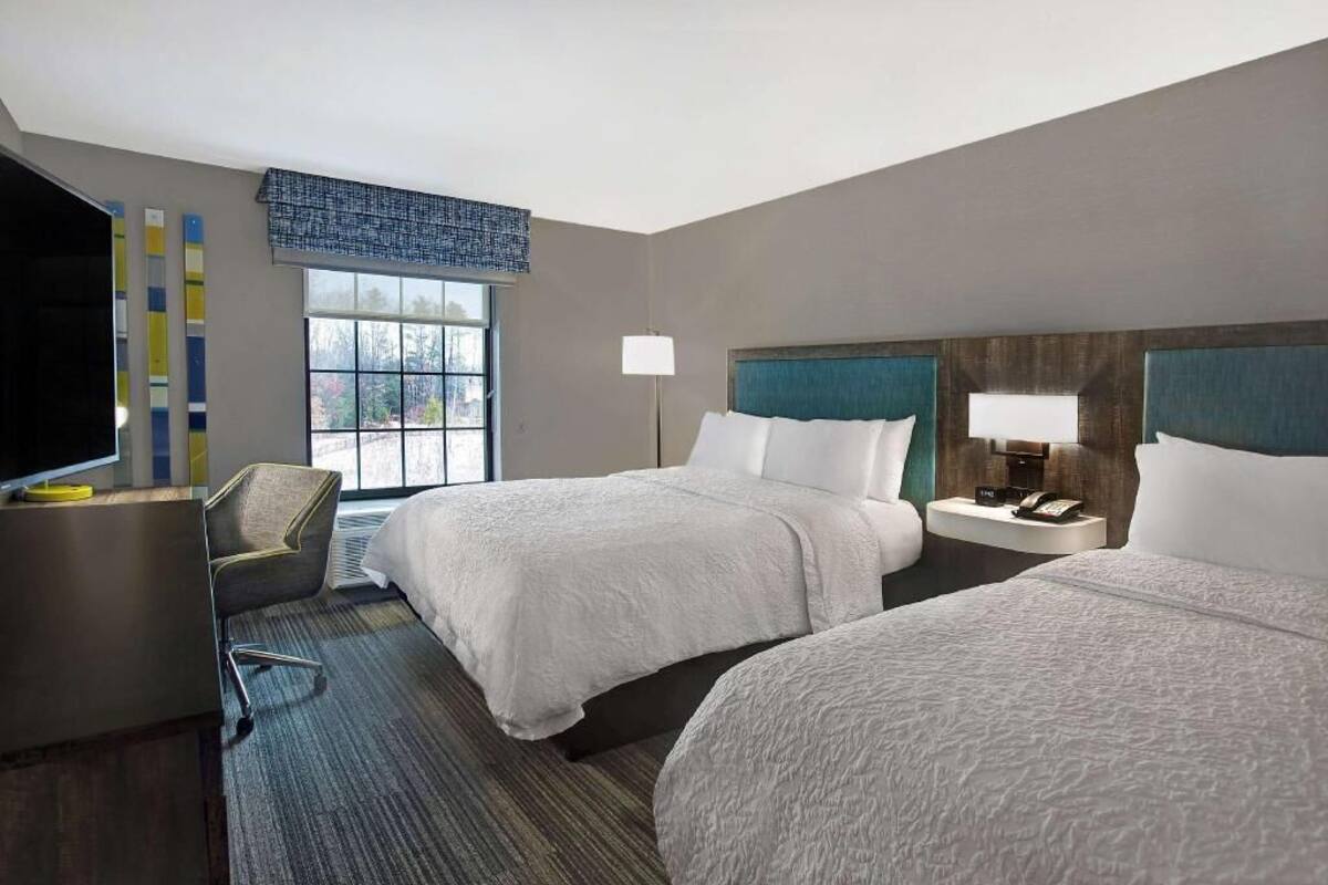 A hotel room with two beds, a desk, a chair, a TV, and a window with a view.