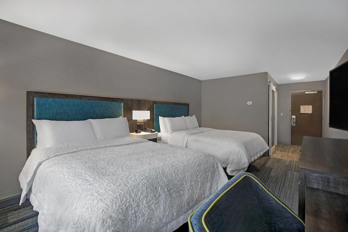 A hotel room with two beds, a desk, a chair, and a television.