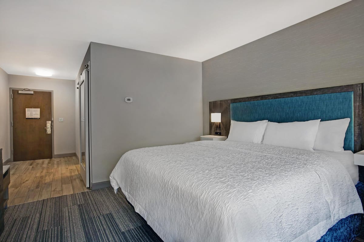 A hotel room with a large bed, a wooden headboard, a nightstand, and a door with a sign.