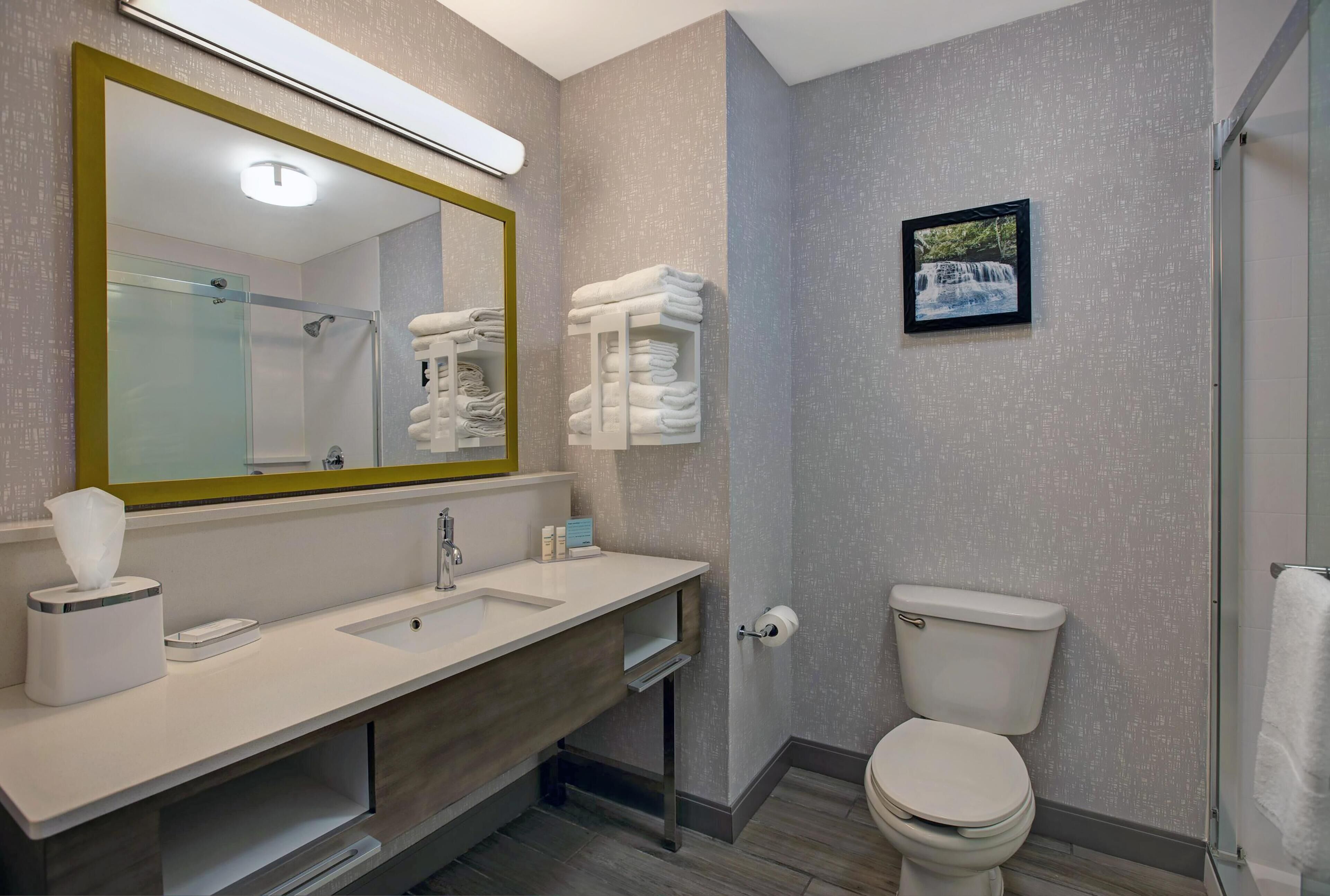 A modern bathroom with a large mirror, a sink, a toilet, and a shower area.