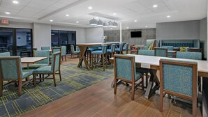 A modern dining area with tables and chairs, a patterned carpet, and a wall-mounted TV.