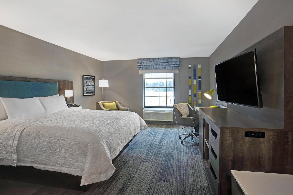 A hotel room with a large bed, a desk, a flat-screen TV, and a window with blinds.