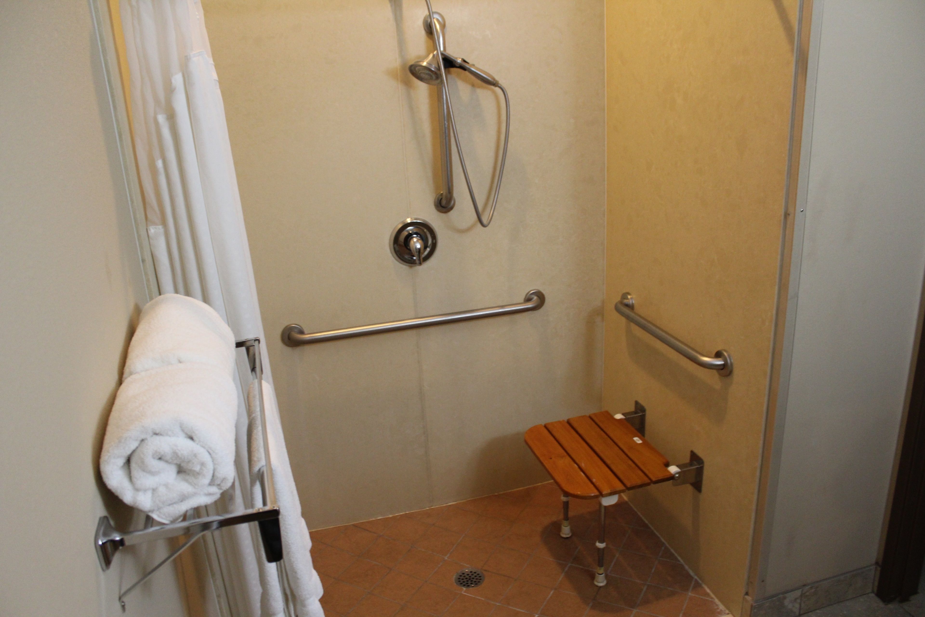 A bathroom with a shower, grab bars, a towel rack, and a bench.