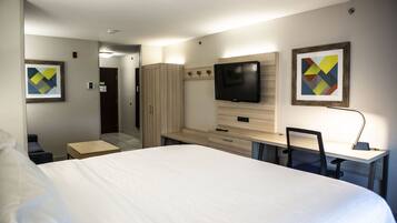 A hotel room with a large bed, a desk with a chair, a TV mounted on the wall, and artwork on the walls.