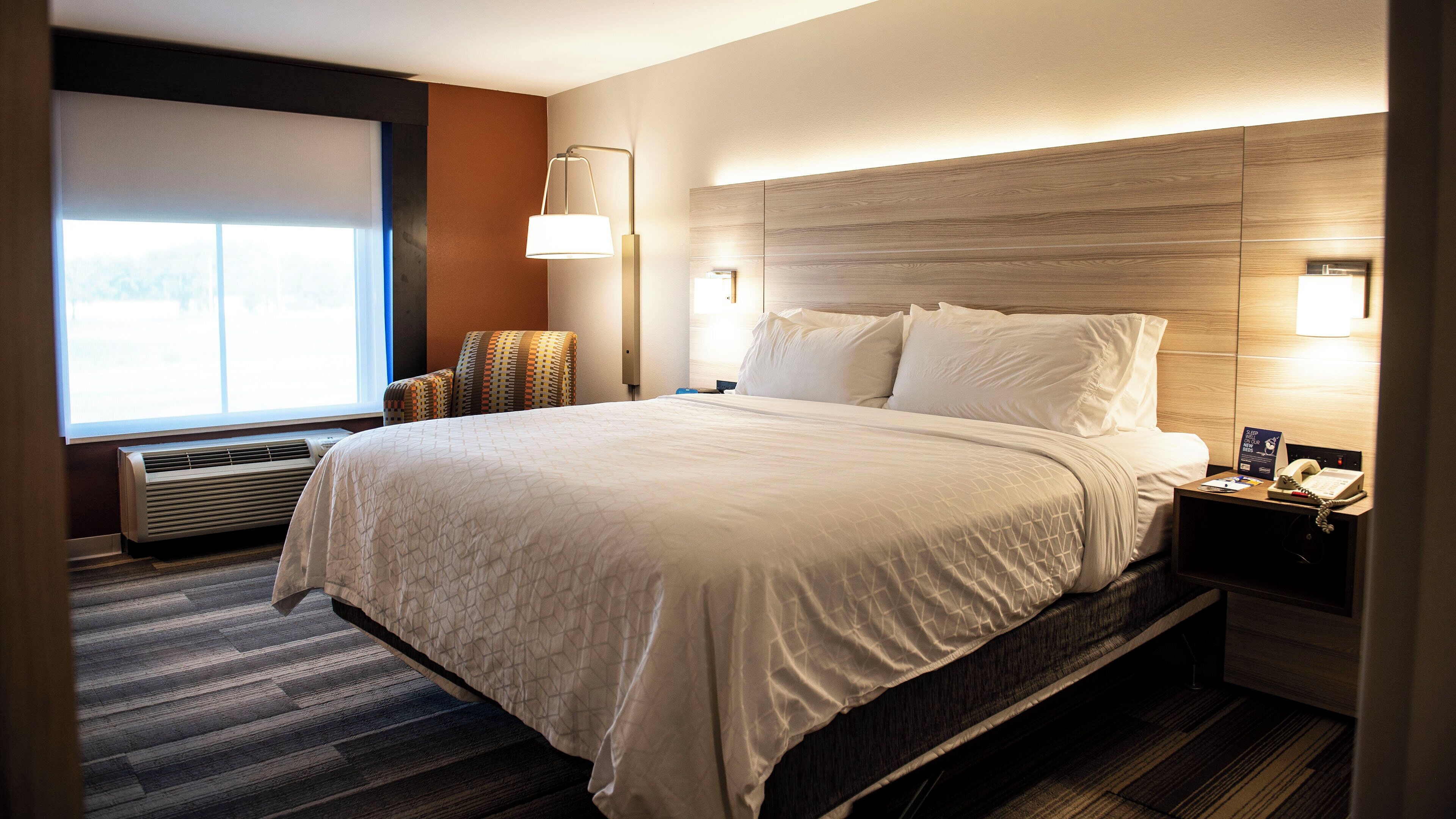 A hotel room with a large bed, bedside lamps, a nightstand, and a window with blinds.