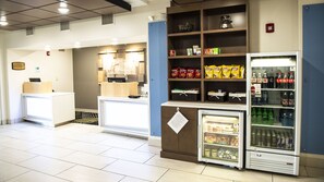 Un espace de restauration propre et bien éclairé, doté d’un comptoir en libre-service, d’une vitrine réfrigérée contenant des aliments surgelés et d’un distributeur de boissons fraîches rempli de sodas.