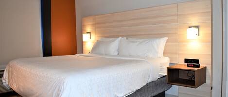 Una habitación de hotel moderna con una cama grande, un cabecero de madera, dos lámparas de noche y una mesita de noche con un reloj.