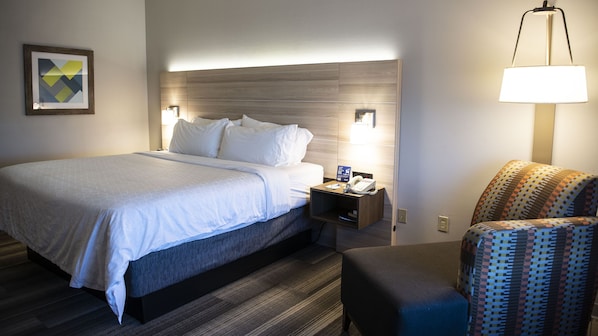 Une chambre d’hôtel avec un lit, une table de chevet, une lampe et un fauteuil à motifs.