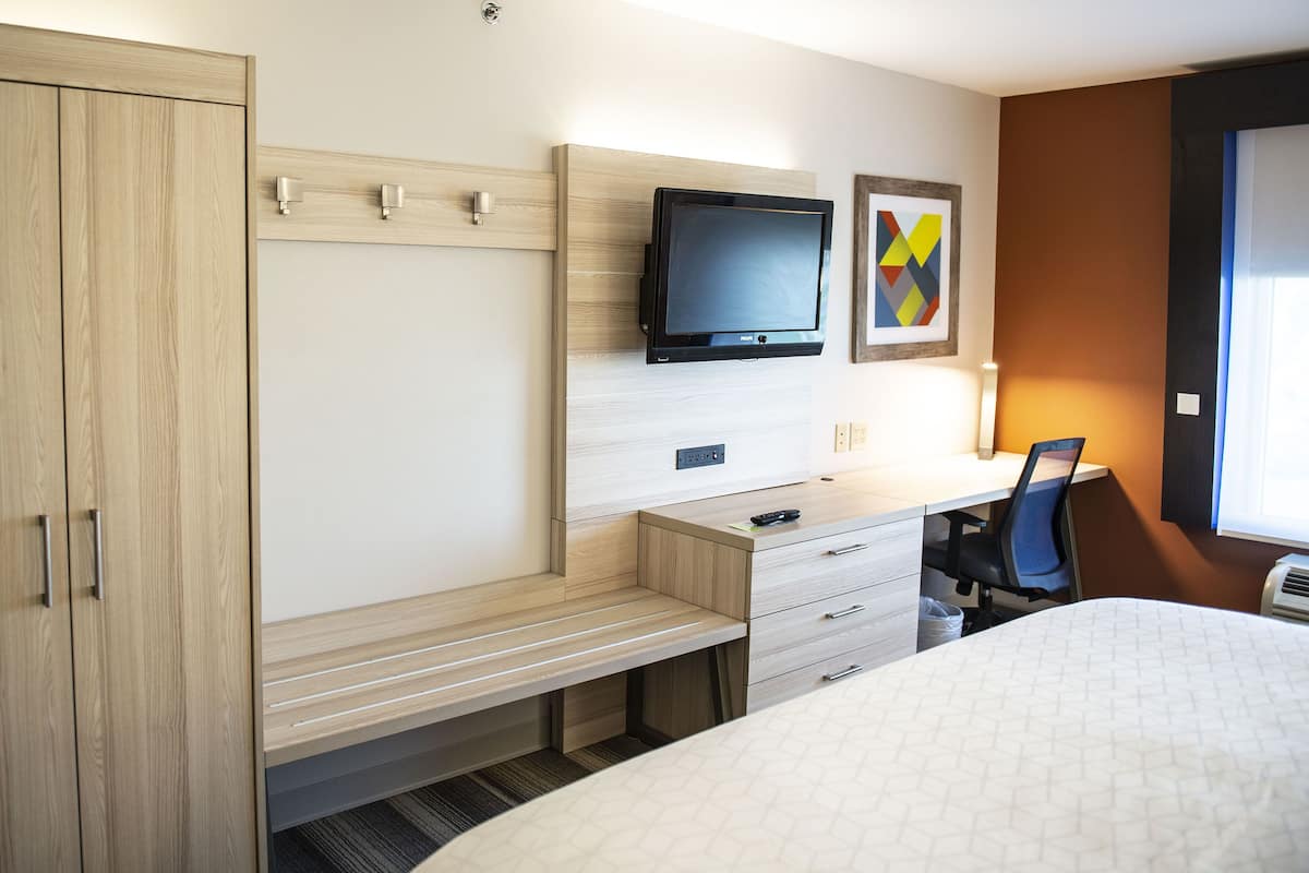 Ein Hotelzimmer mit Bett, Schreibtisch, Stuhl, Fernseher und Kleiderschrank.