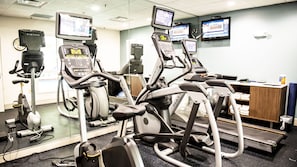 Une salle de sport équipée de nombreux appareils de cardio, notamment des tapis de course et des vélos d’appartement, et dotée d’un mur recouvert de miroirs.
