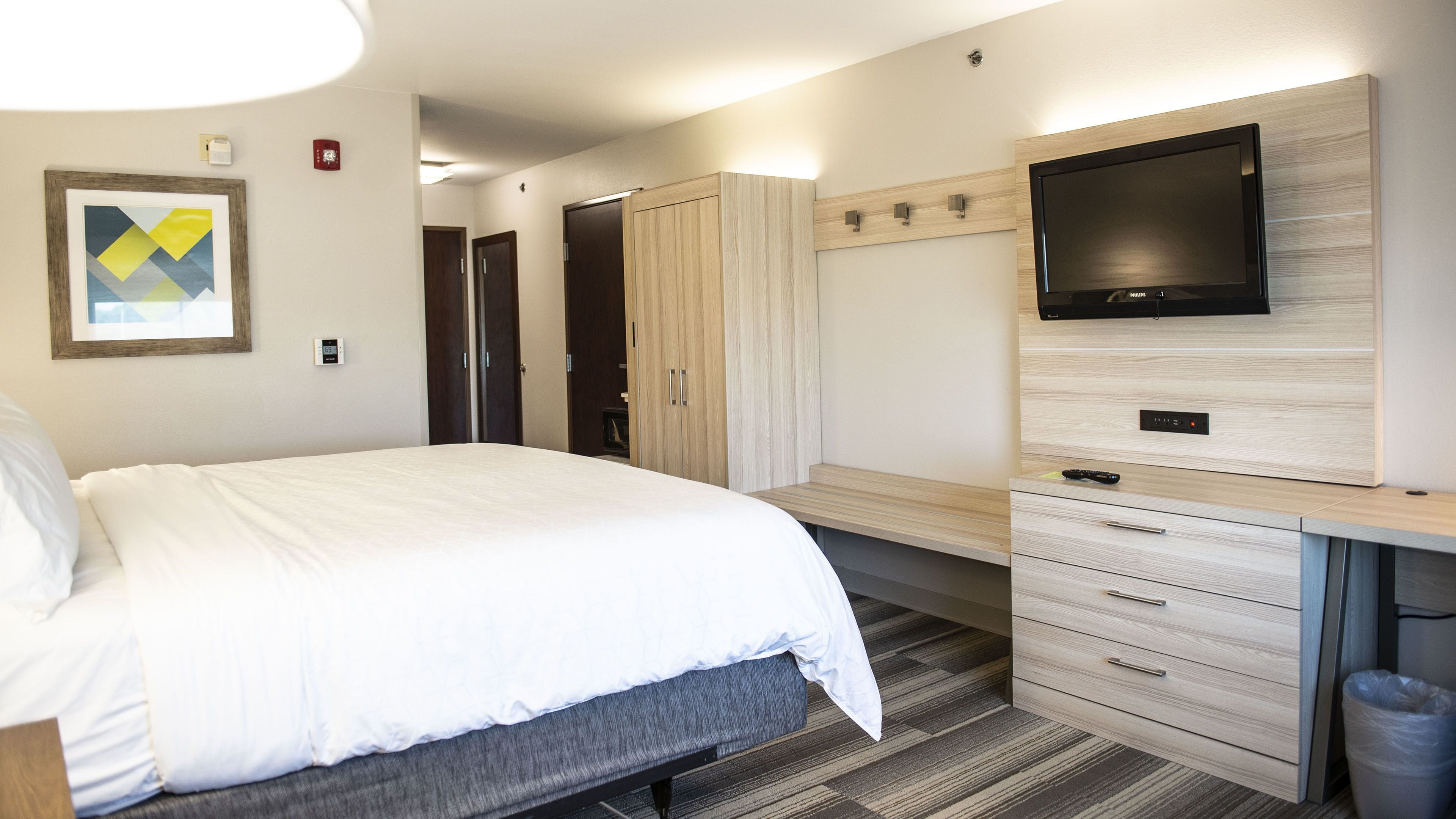 Habitación de hotel con cama, escritorio con cajones, televisor de pantalla plana y armario.