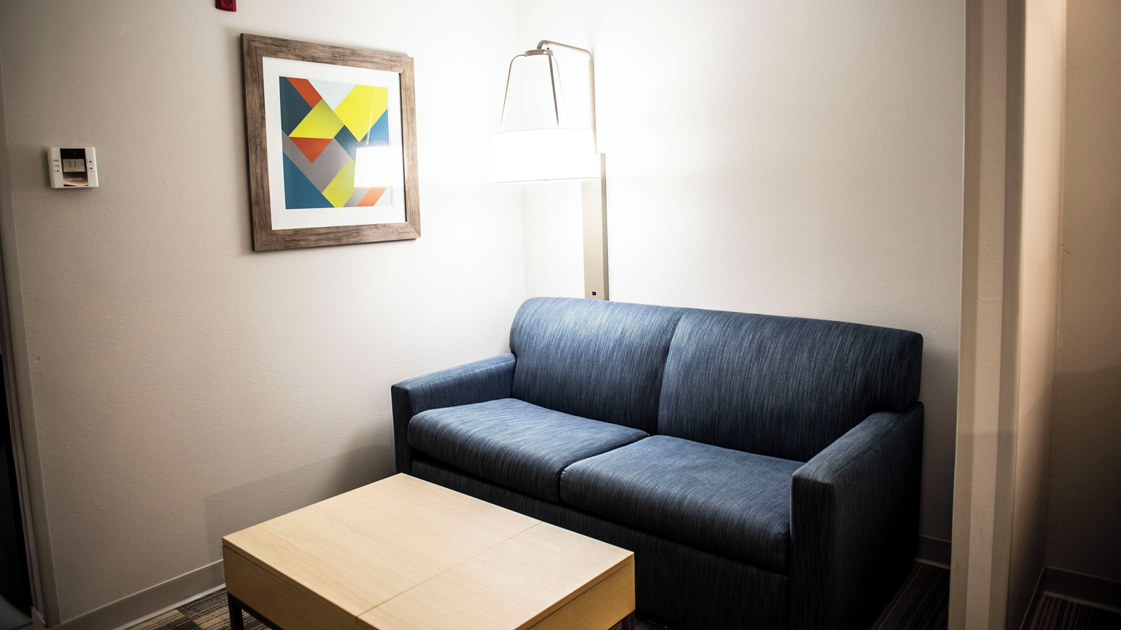 Ein Zimmer mit einem blauen Sofa, einem kleinen Holztisch, einem gerahmten geometrischen Kunstwerk und einer Stehlampe.
