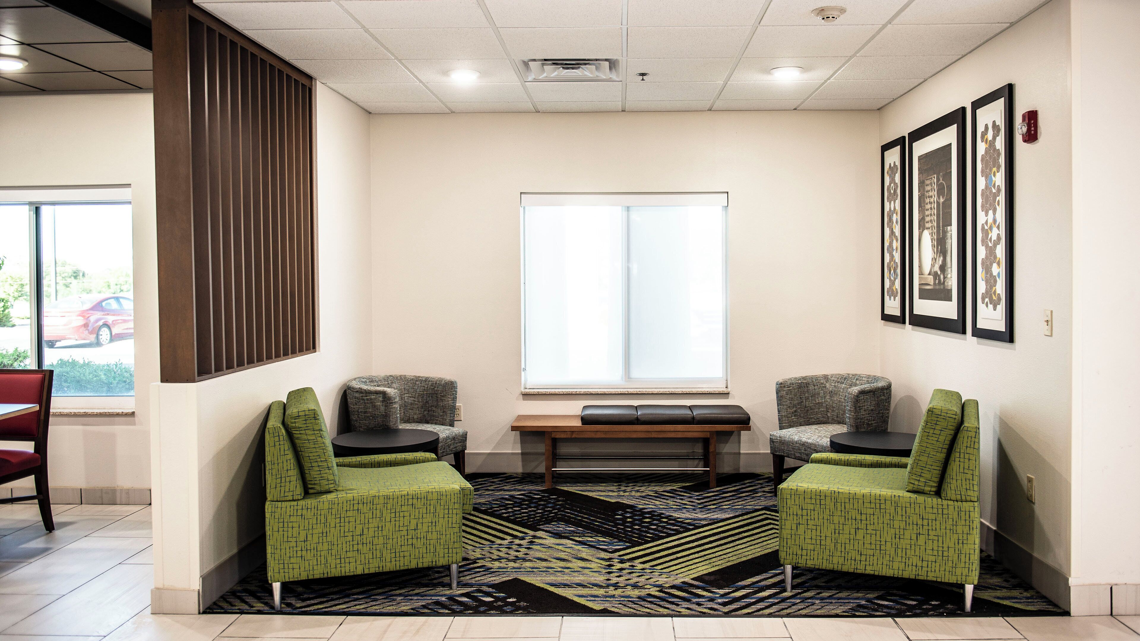 A waiting area with two green armchairs, a bench, and a patterned rug.