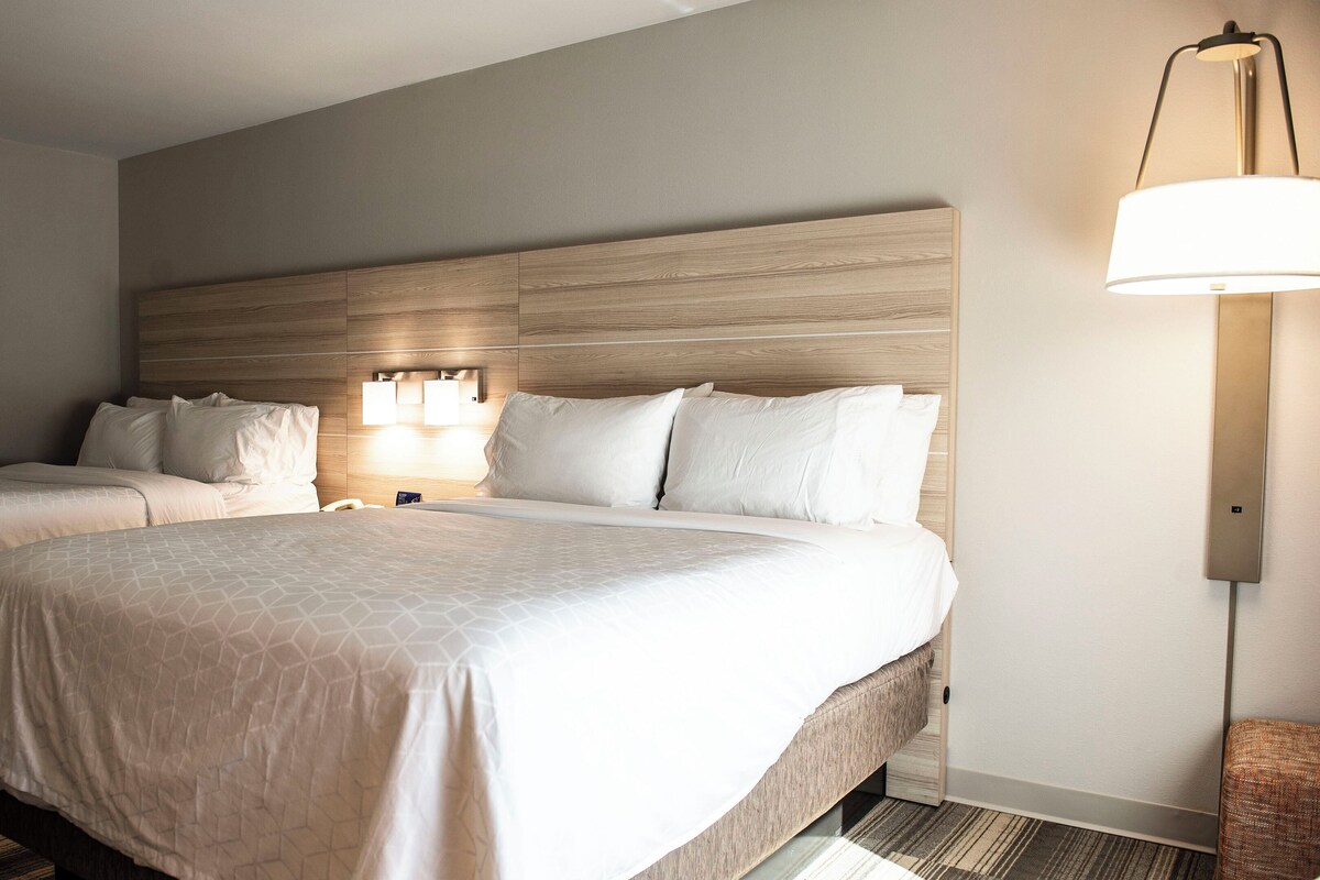 A hotel room with two beds, a headboard, bedside lamps, a framed picture on the wall, and a floor lamp.