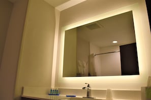 Une salle de bain avec un grand miroir, un lavabo et un porte-serviettes.
