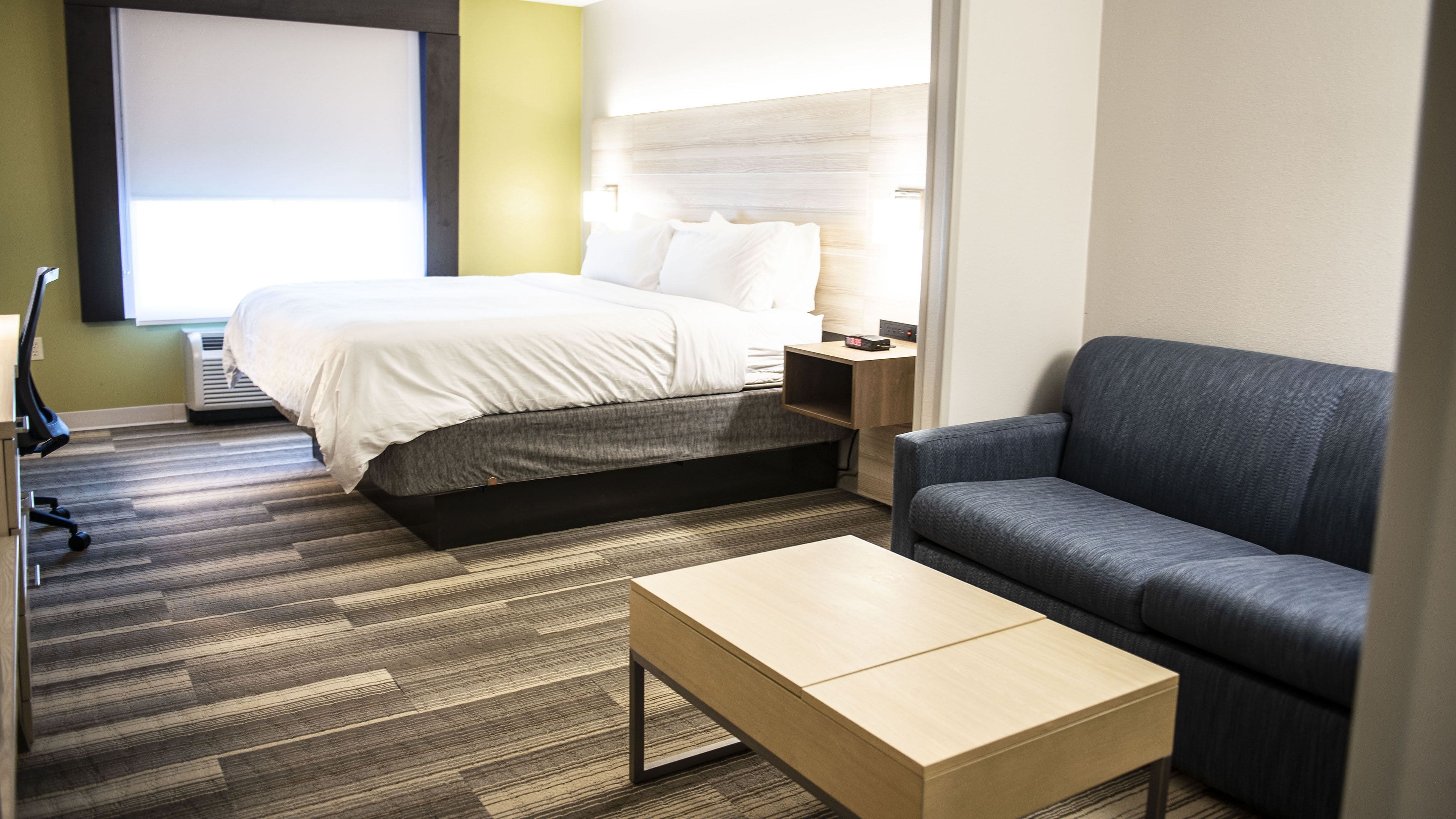 A hotel room with a bed, a sofa, a coffee table, and a desk with a lamp.