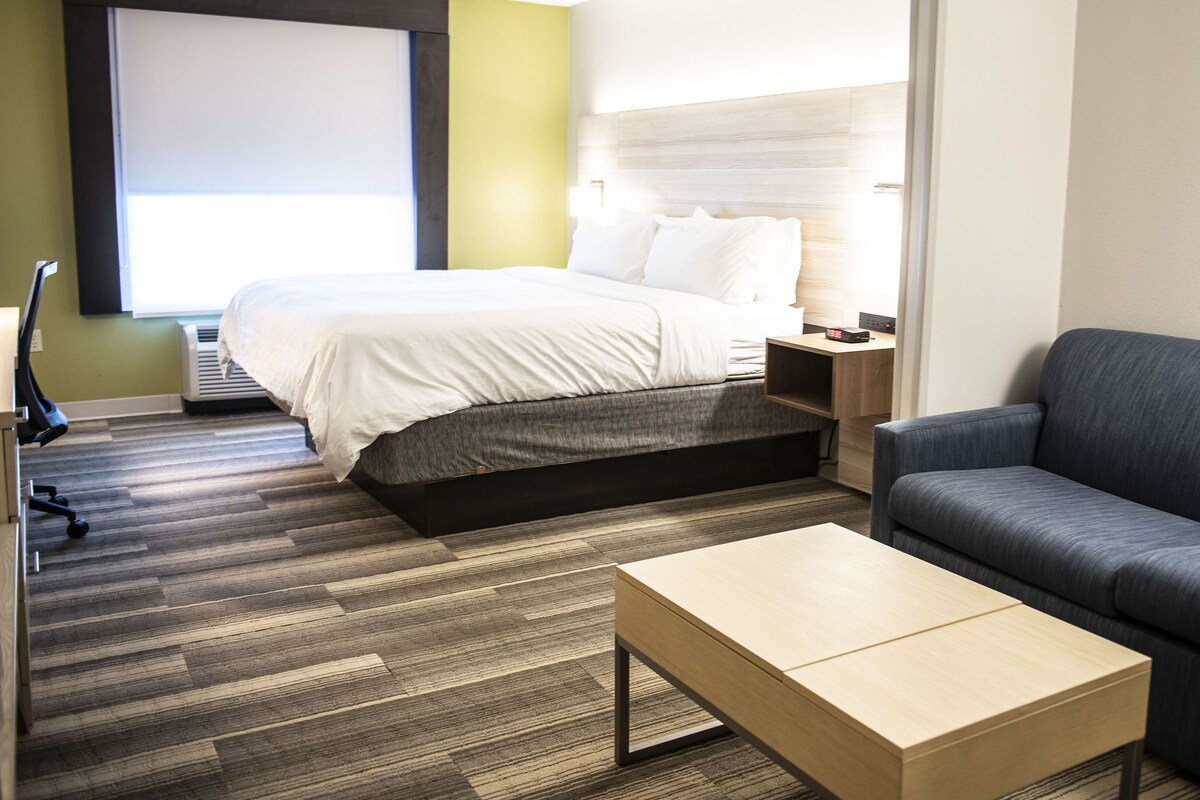 A hotel room with a bed, a sofa, a coffee table, and a desk with a lamp.