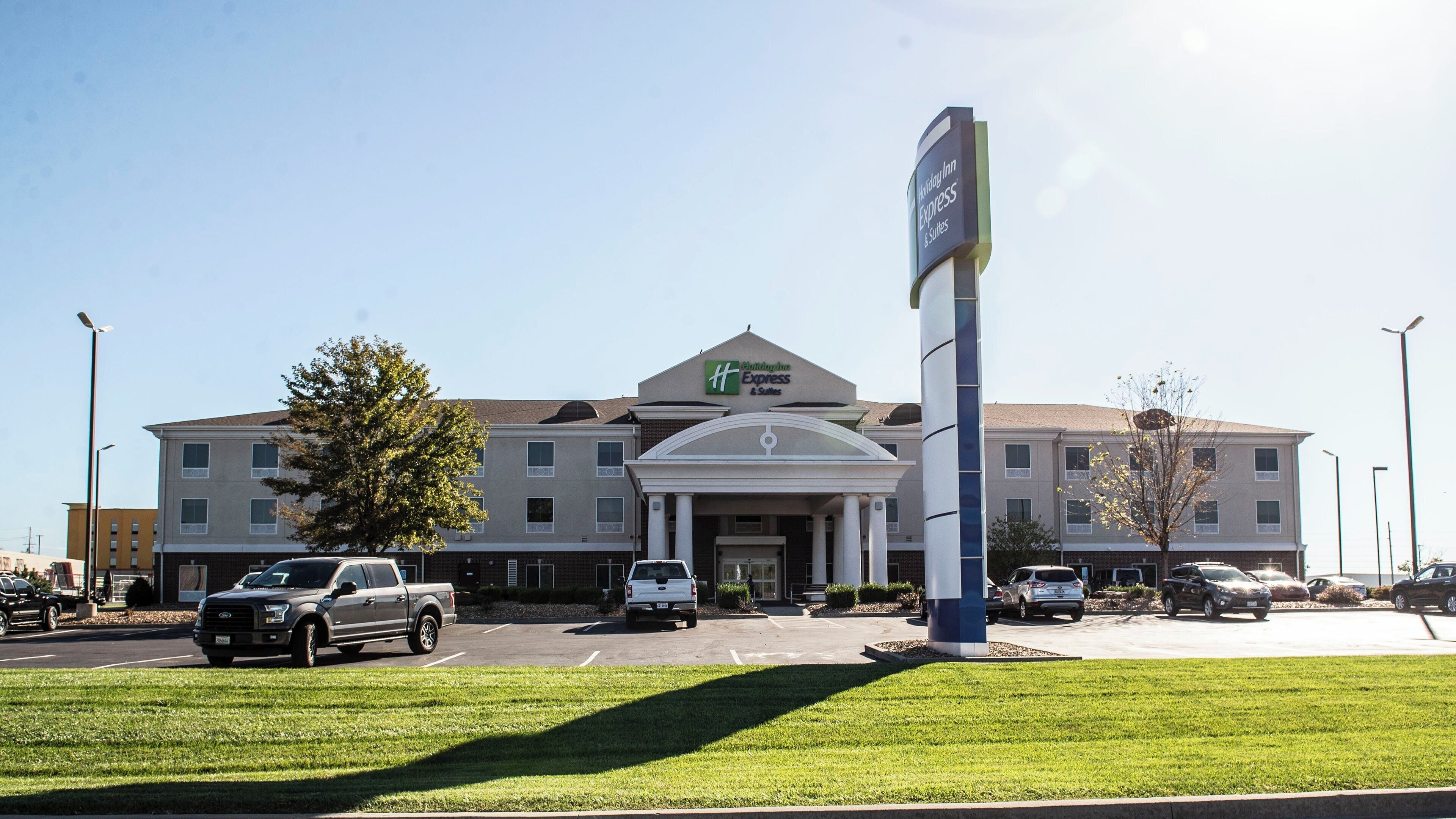Un hotel Holiday Inn Express & Suites con entrada principal, estacionamiento y zonas verdes circundantes.