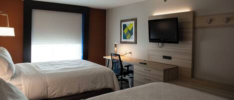 Ein Hotelzimmer mit zwei Betten, einem Schreibtisch mit Stuhl, einem Fernseher und einem Fenster mit Jalousien.