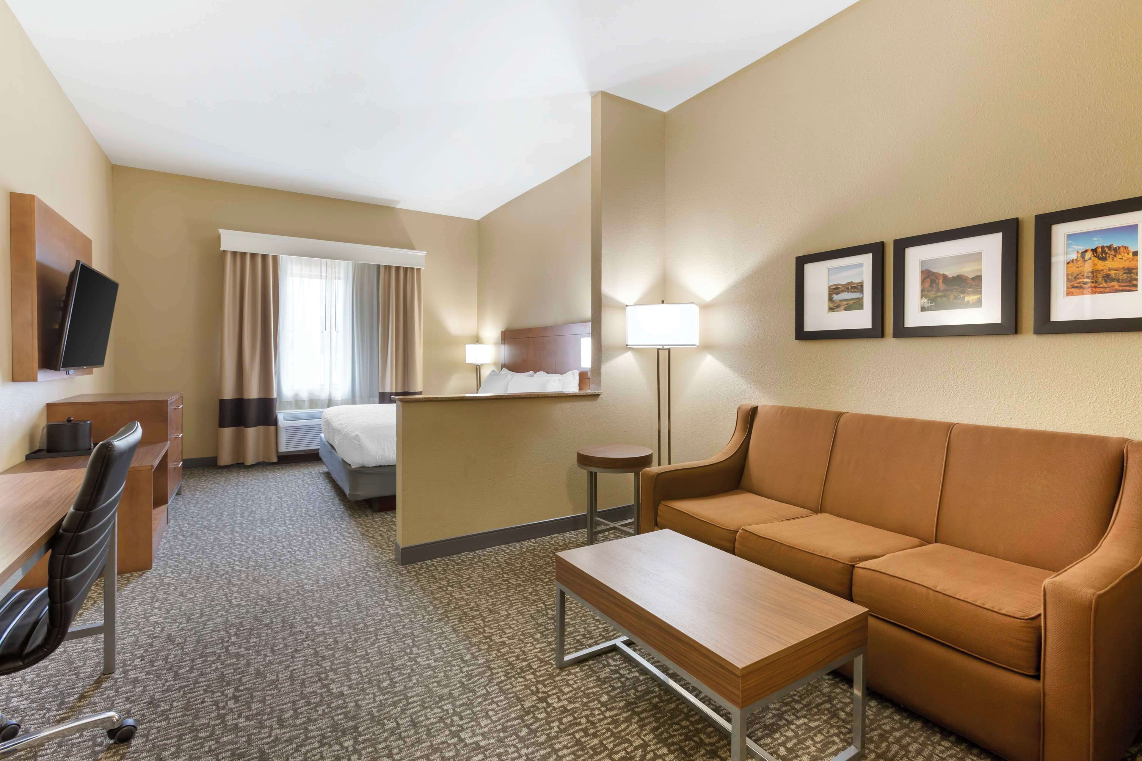 Habitación de hotel con cama, sofá, escritorio, silla, televisor y cuadros en la pared.