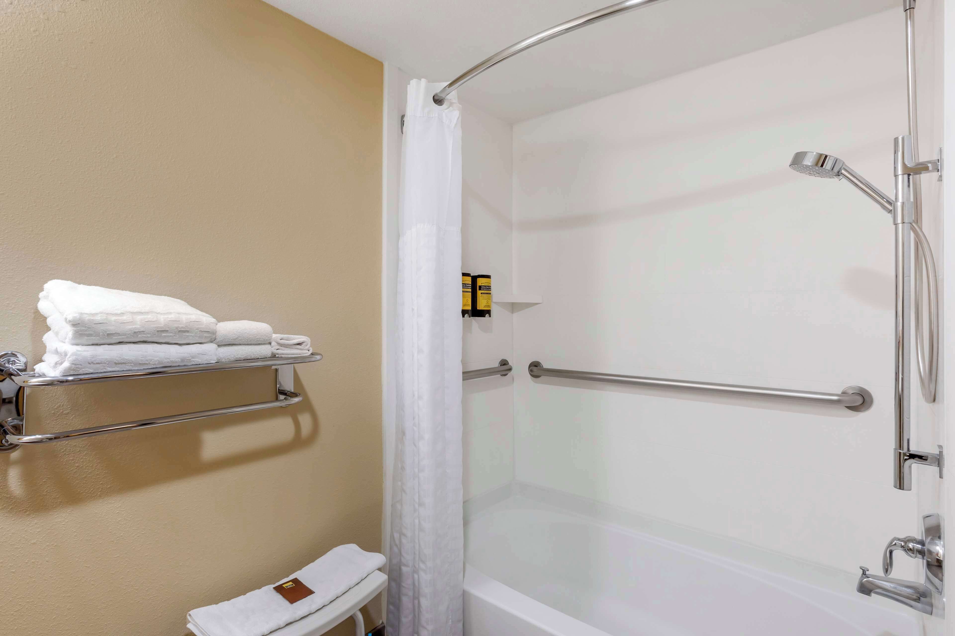 A bathroom with a glass-enclosed shower, a towel rack with folded towels, and a toilet with a towel on it.