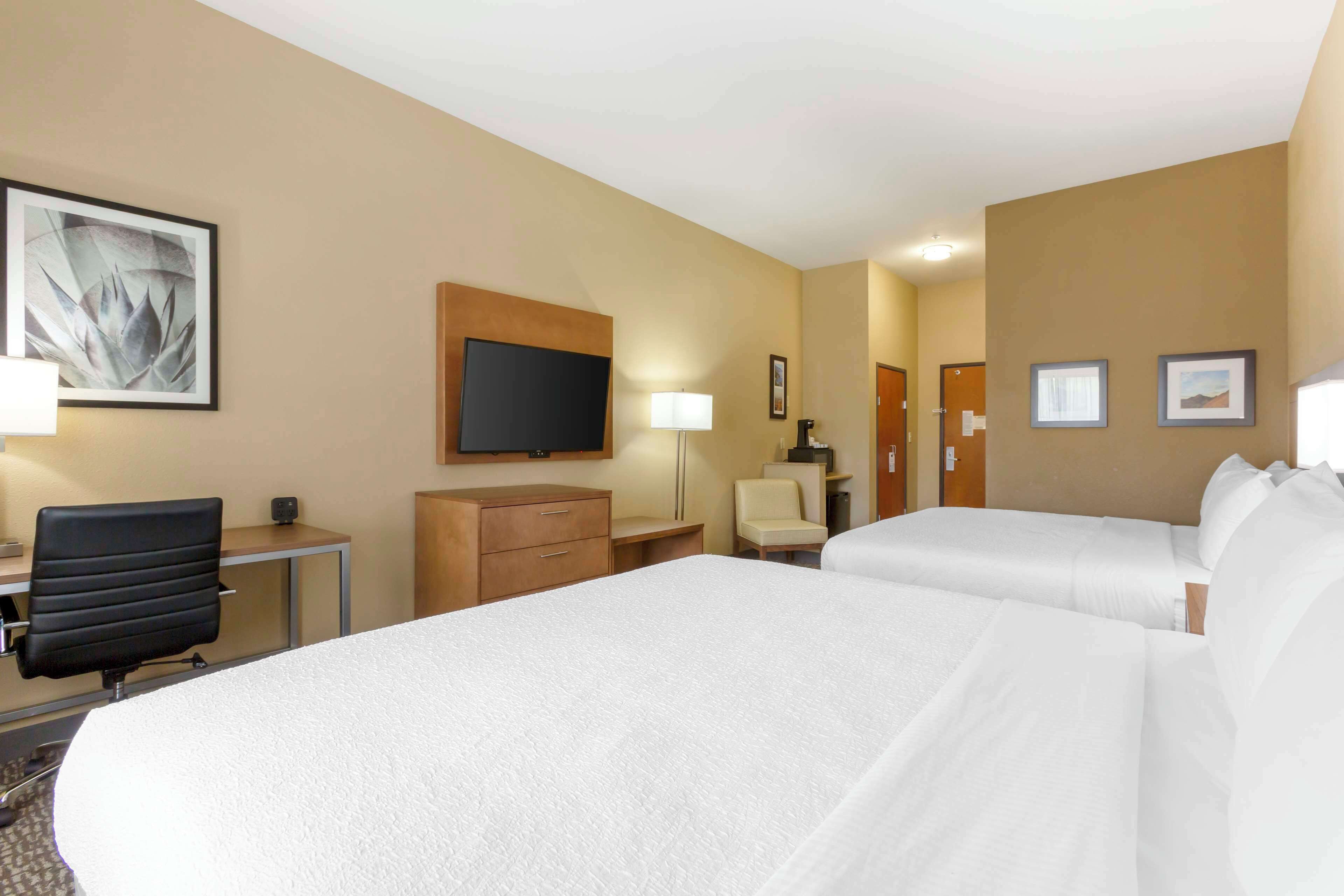 A hotel room with two beds, a desk with a chair, a TV, and a lamp.