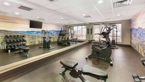 Een fitnessruimte met cardioapparaten, gewichtbanken en dumbbells.