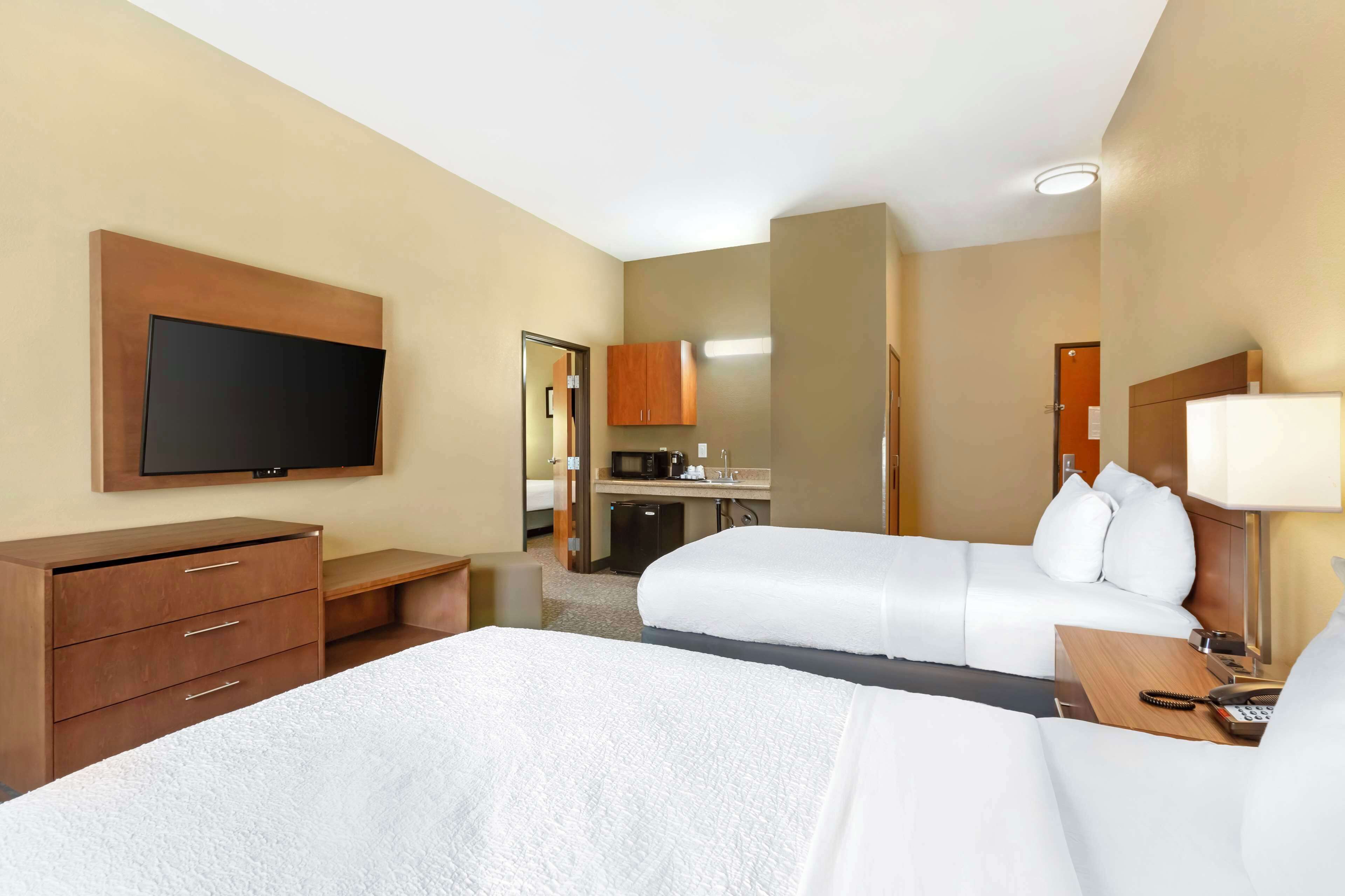 Habitación de hotel con dos camas, televisión, escritorio, microondas y baño visible a través de una puerta abierta.