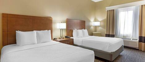 A hotel room with two beds, a wooden headboard, bedside lamps, a telephone, and a window with curtains.