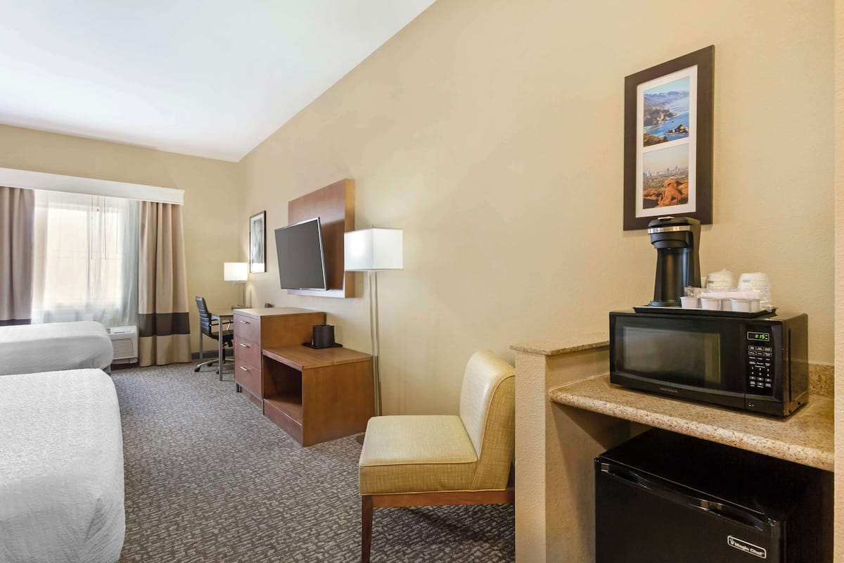 A hotel room with a bed, a desk, a chair, a microwave, a coffee maker, and a television.