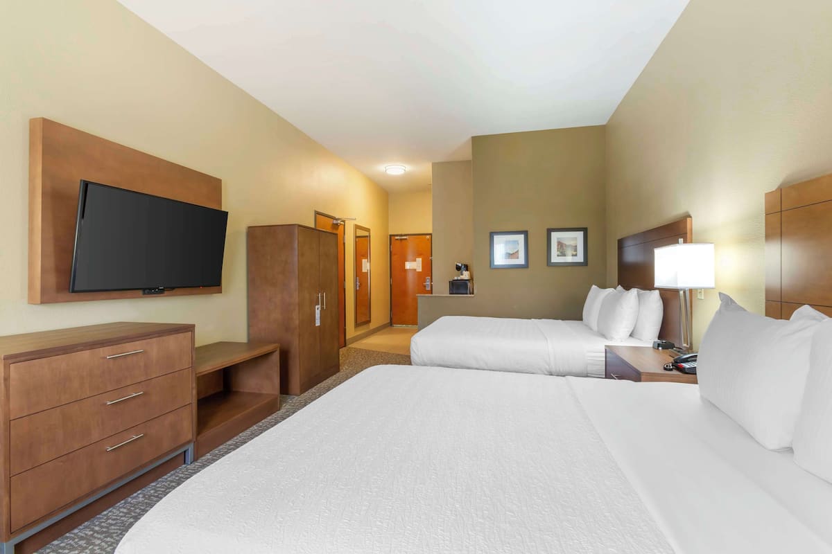 A hotel room with a large bed, a TV mounted on the wall, a desk with a lamp, and a wardrobe.