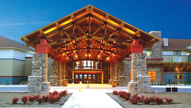 A building with a stone facade, a wooden covered entrance, and a clear sky. - Kewadin Casinos St. Ignace Hotel (St Ignace)