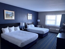 Habitación de hotel con dos camas, un escritorio, una silla, una lámpara, un teléfono y un cuadro en la pared.