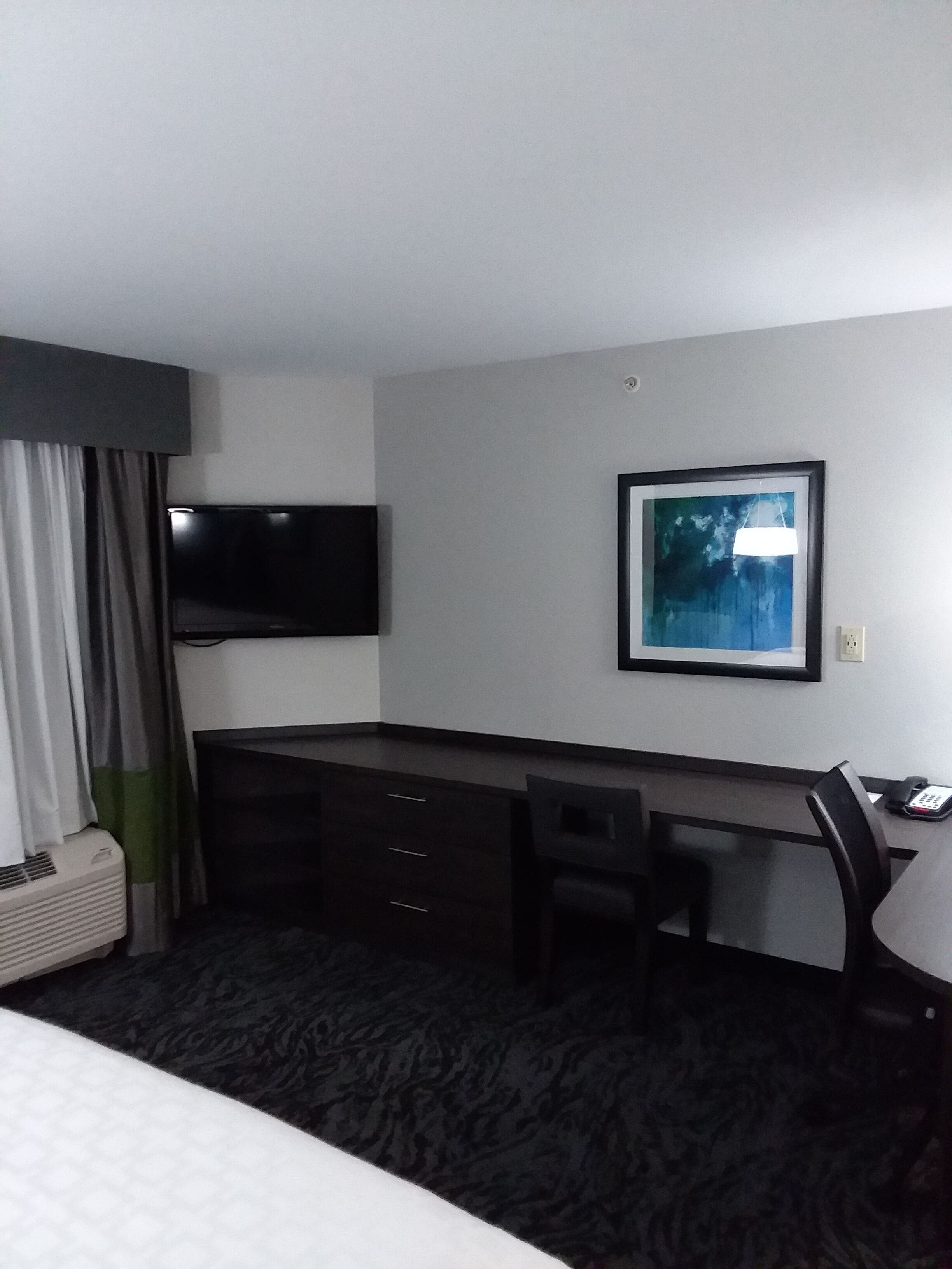Una camera d'albergo con un letto, una scrivania con una sedia, una TV a schermo piatto, un quadro appeso al muro e un telefono.