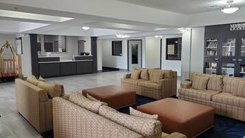 Un moderno vestíbulo de hotel con recepción, zona de estar con sofás y otomanas, un espejo grande y una estantería.