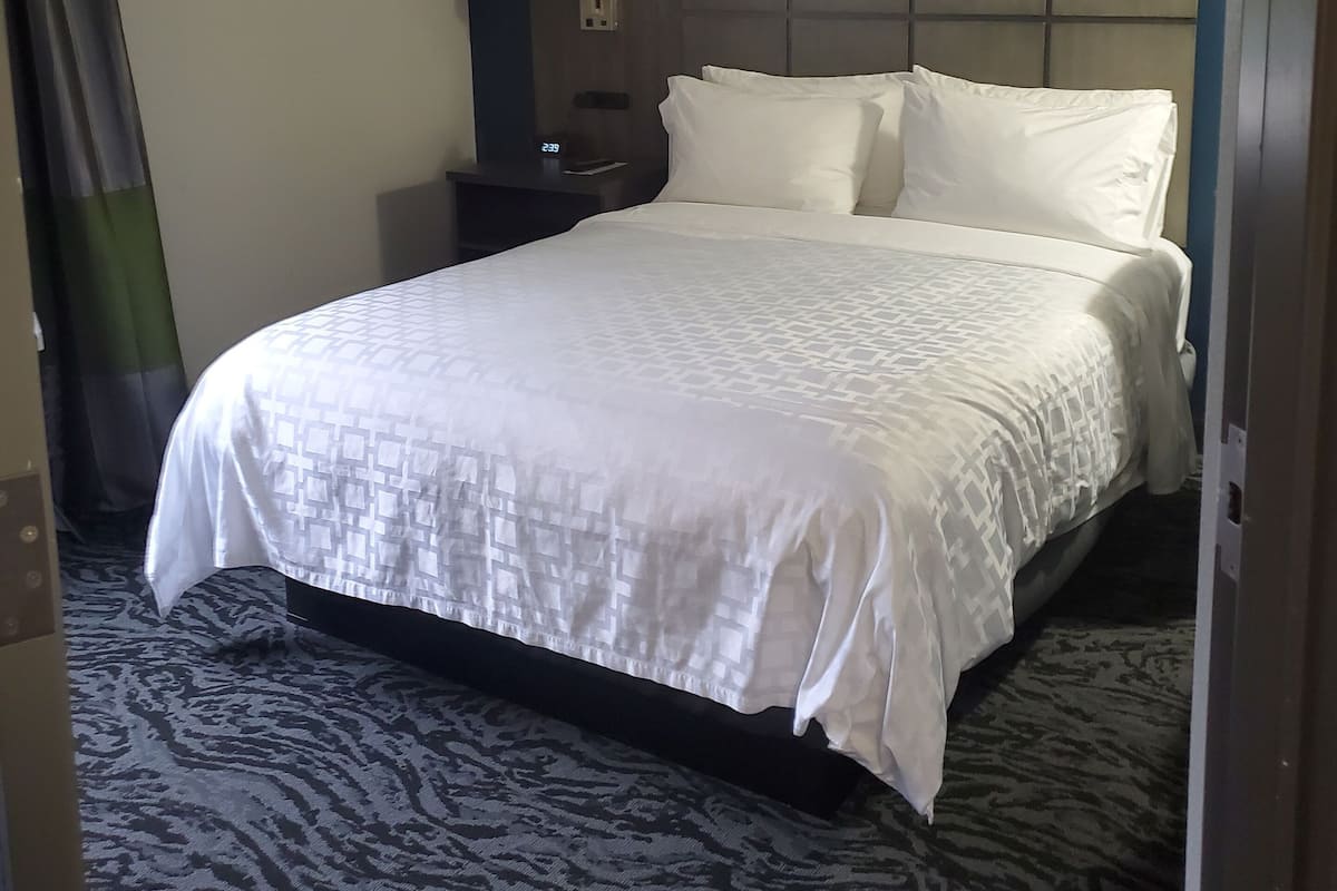 Une chambre d’hôtel avec un grand lit, une table de chevet, une lampe et une tête de lit.