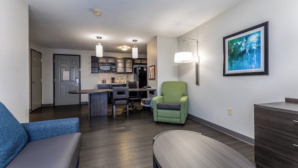 A modern living room with a sofa, a dining table, and a kitchen area in the background. - Candlewood Suites Knoxville Airport-Alcoa by IHG (Alcoa)