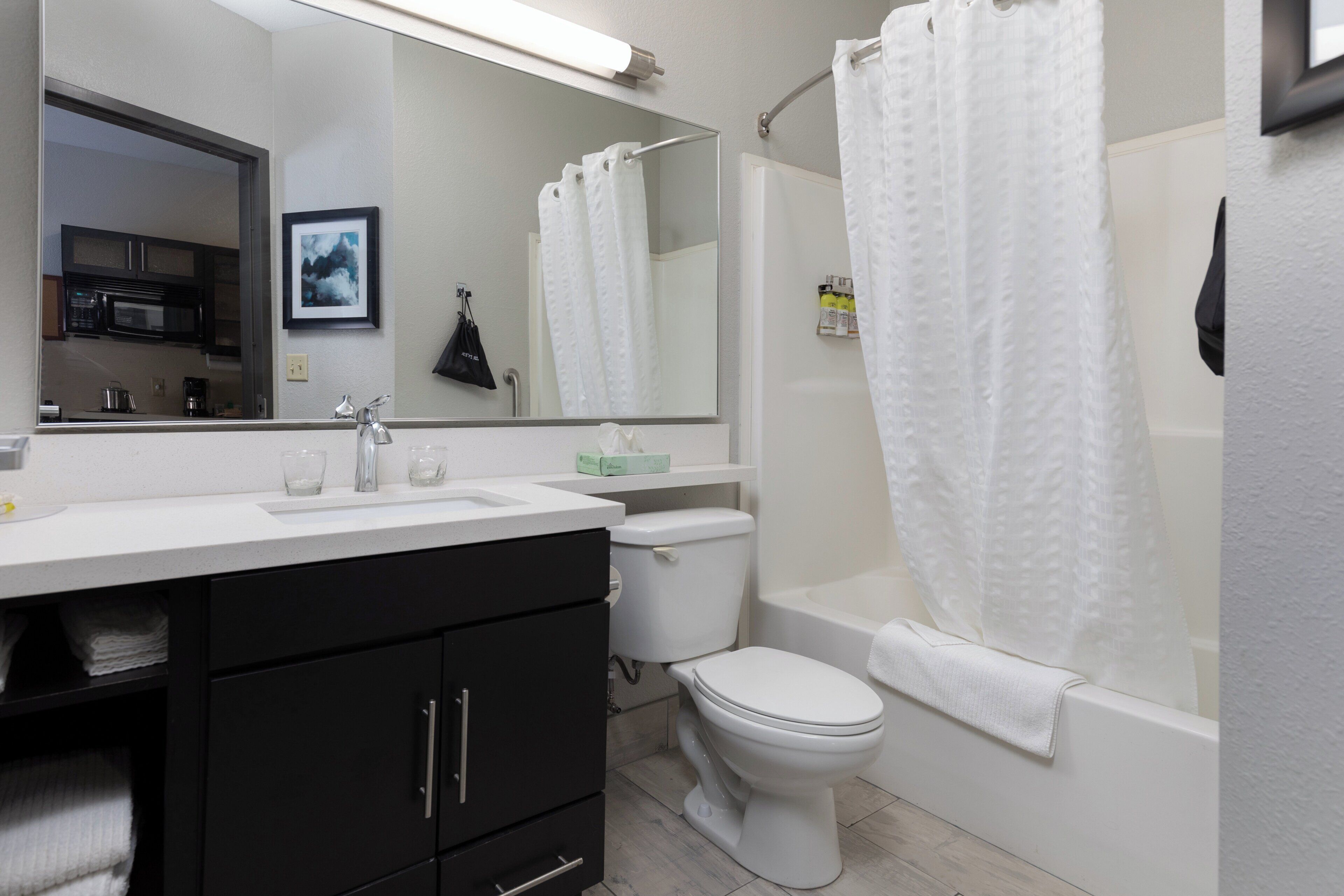 A modern bathroom with a white sink, black cabinets, a toilet, and a bathtub with a shower curtain.