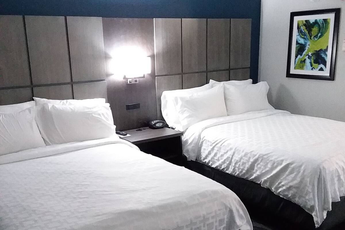 Une chambre d’hôtel avec deux lits, une table de chevet, une lampe et un tableau au mur.