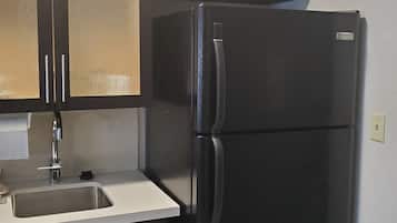 A kitchen with a black refrigerator, a sink, and dark cabinets.