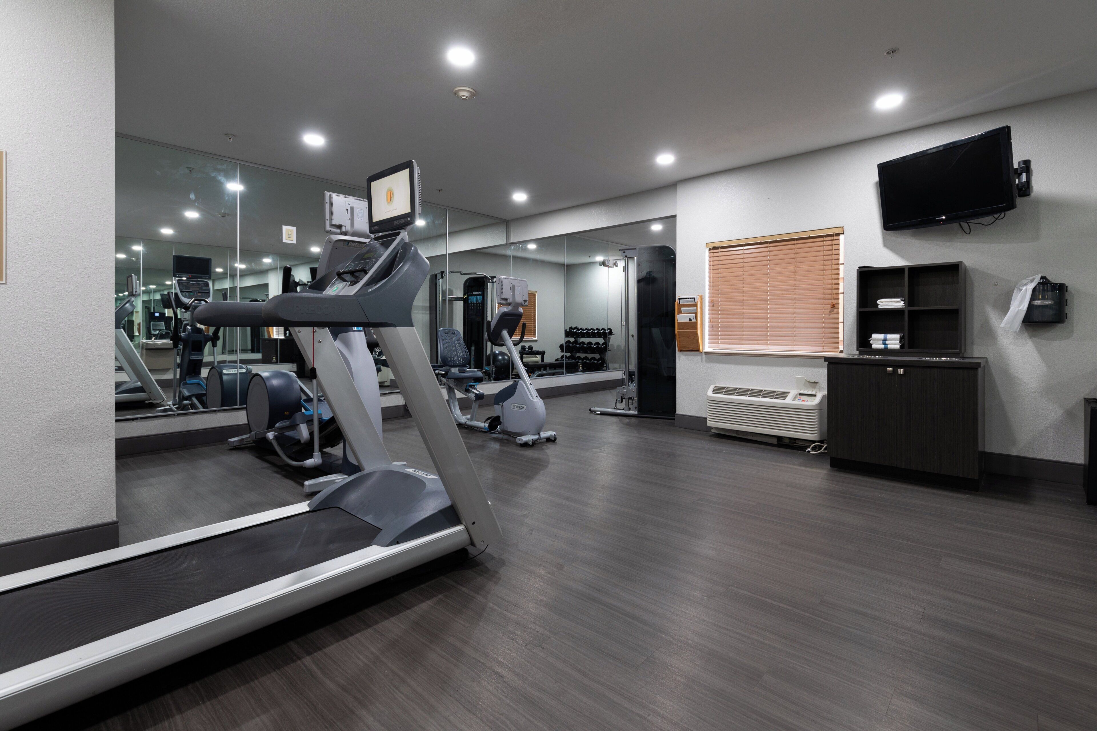 Un gimnasio con equipamiento de ejercicio, un espejo, un televisor y una ventana con persianas.