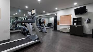Un gimnasio con equipamiento de ejercicio, un espejo, un televisor y una ventana con persianas.