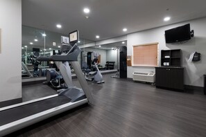 A gym with exercise equipment, a mirror, a television, and a window with blinds.