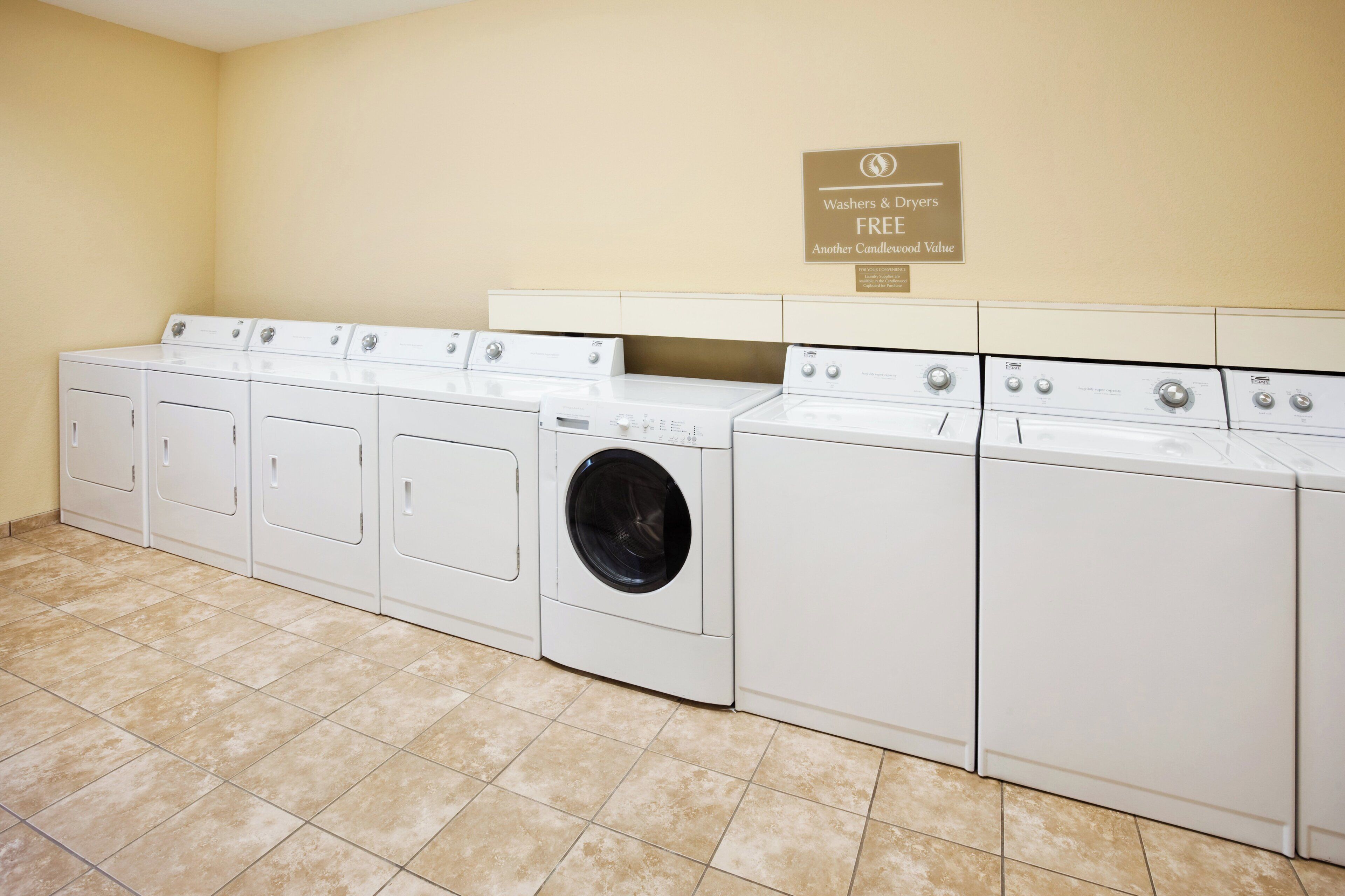 A laundry facility with multiple washers and dryers, a sign indicating free use, and a tiled floor.