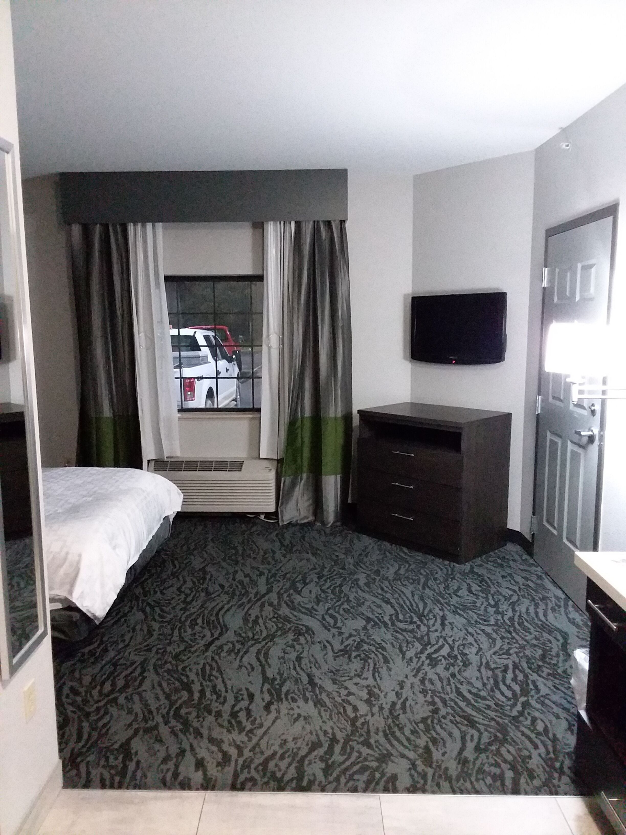 A hotel room with a bed, a dresser, a television, and a window with curtains.