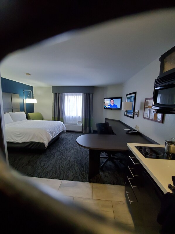 A hotel room with a bed, a desk, a television, and a kitchenette.