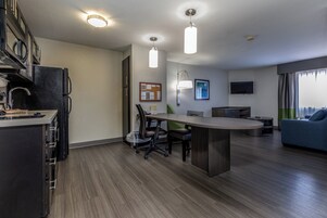 A modern kitchen with a built-in refrigerator, a dining area with a central island, and a living space with a sofa and a flat-screen TV.