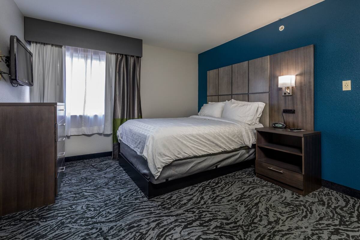 Une chambre d’hôtel avec un lit, une table de chevet, une télévision et une fenêtre avec des rideaux.