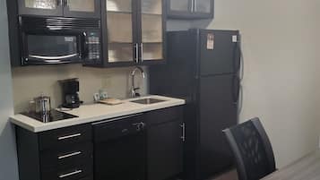 A compact kitchen with dark cabinetry, a microwave, a refrigerator, and a sink.